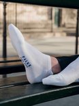 Man met witte FALKE Cool Kick sokken en sneakers zittend op een bankje.