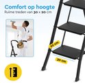 Man op een zwarte metalen huishoudtrap met 3 treden die een plafond schildert.