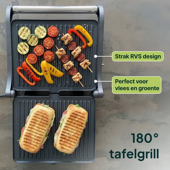 Open contactgrill met gegrilde groenten en spiesjes boven, en twee panini's onder. "180° tafelgrill", "Strak RVS design", "Perfect voor vlees en groente".