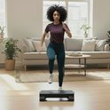 Vrouw met krullend haar in sportkleding, traint op een zwarte aerobic step met dumbbells.