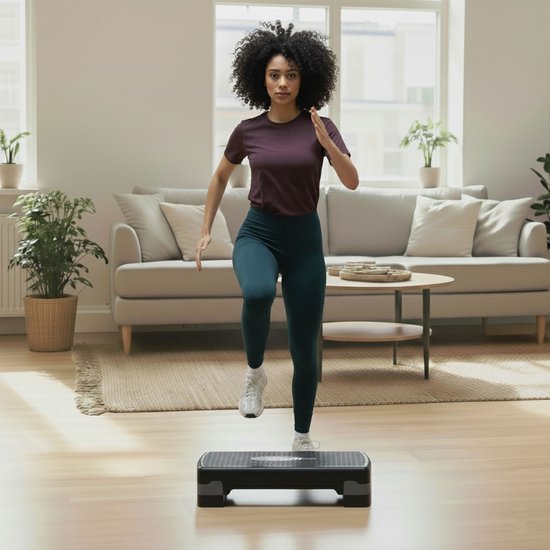 Vrouw met krullend haar in sportkleding, traint op een zwarte aerobic step met dumbbells.