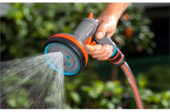 Een hand houdt een grijze Gardena sproeikop met oranje accenten vast, waar water uitspuit.