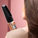 Close-up van een vrouw met bruin haar, gebruikt het mondstuk van een gouden stylingborstel.