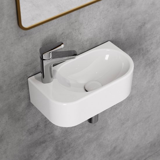 Petit lavabo blanc en céramique avec robinetterie chromée, monté sur le mur, avec un miroir au-dessus.
