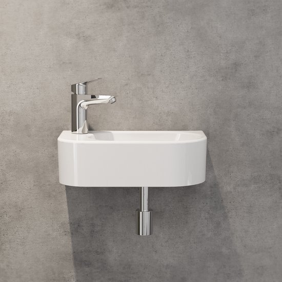 Wit keramieken fonteintje aan een betonnen muur met een chromen kraan en afvoerbuis.