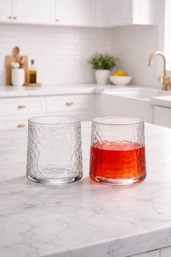 Deux verres transparents martelés sur un comptoir en marbre, dont un rempli d'une boisson rouge.