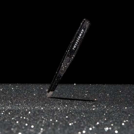Zwarte glitter Tweezerman pincet schuin op een glinsterende ondergrond.