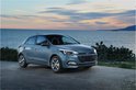 Blauwe Hyundai i20 hatchback met koplampen aan, geparkeerd aan de kust bij zonsondergang.