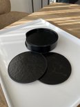 Zwarte ronde onderzetters met marmerprint, twee liggen los naast de stapel in de zwarte houder op een witte schaal.