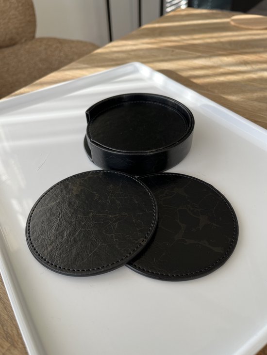 Zwarte ronde onderzetters met marmerprint, twee liggen los naast de stapel in de zwarte houder op een witte schaal.