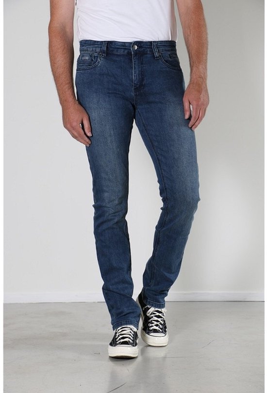 Voorkant van een man in een blauwe spijkerbroek met slim fit, stone used wassing en zwarte sneakers.
