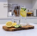 Glazen fles met citroen en komkommer, naast een glas water op een houten plank.