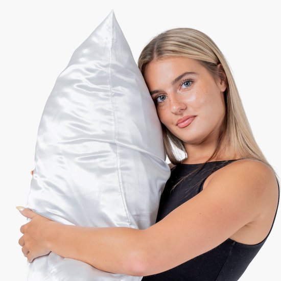 Blonde vrouw met blauwe ogen omhelst een grote satijnen kussensloop in het wit.