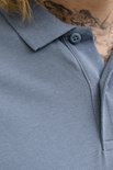 Close-up van een blauwgrijze poloshirt met een knoopsluiting en kraag. Een deel van een tatoeage is zichtbaar.