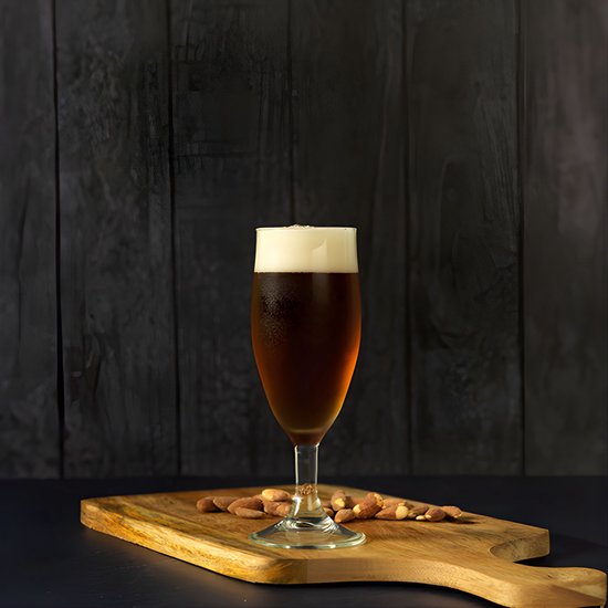 Een glas donker bier met een dikke schuimkraag staat op een houten plank met amandelen, tegen een donkere achtergrond.