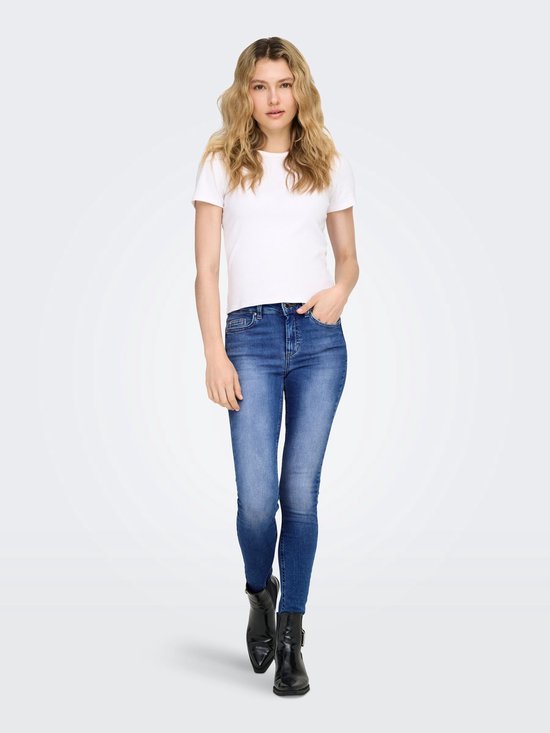 Model draagt een skinny jeans met blauwe denim wassing en rafelige zoom, gecombineerd met zwarte laarsjes.