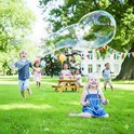 Kinderen maken in de tuin reuze zeepbellen met houten stokken en touw. Er is een picknicktafel met taart en slingers.