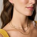 Gouden collier met kleine hartjes en steentjes, gedragen op een gele top.