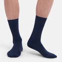 De benen van een man met donkerblauwe, halfhoge sokken. De sokken hebben een gladde afwerking.