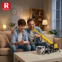 Een vader en zoon zitten op de bank en spelen met een gele en witte mobiele kraanbouwset.