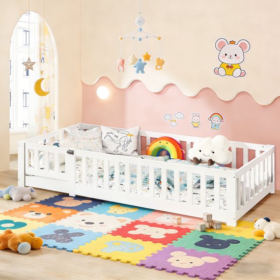 Wit kinderbed met spijlenhek, speelgoed en een kleurrijke speelmat.