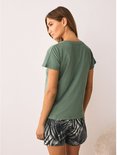 Vrouw in een groen V-hals T-shirt en een short met bladerenprint, kijkend weg.