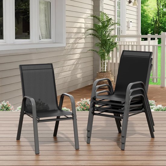 Twee zwarte tuinstoelen, waarvan één stapel, op een houten terras bij een witte woning.