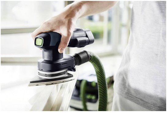 Hand met een Festool schuurmachine met stofzuigerslang die op een witte tafel schuurt.
