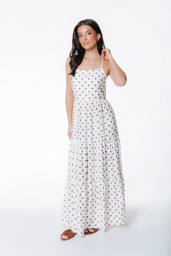 Femme portant une longue robe blanche à pois marron et fines bretelles.