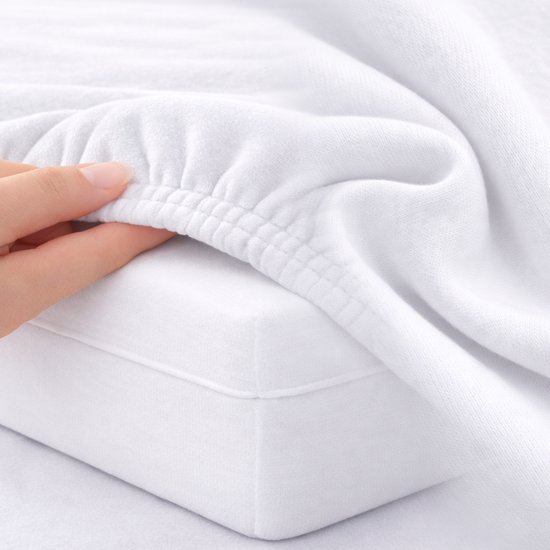 Vinger trekt aan de elastische rand van een wit jersey hoeslaken op een matras.