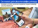 Hand met smartphone toont printapp op een bureau met foto's.