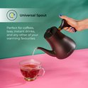 Hand die zwarte CHiATO waterkoker met gouden accent vasthoudt, schenkt water in een glas.