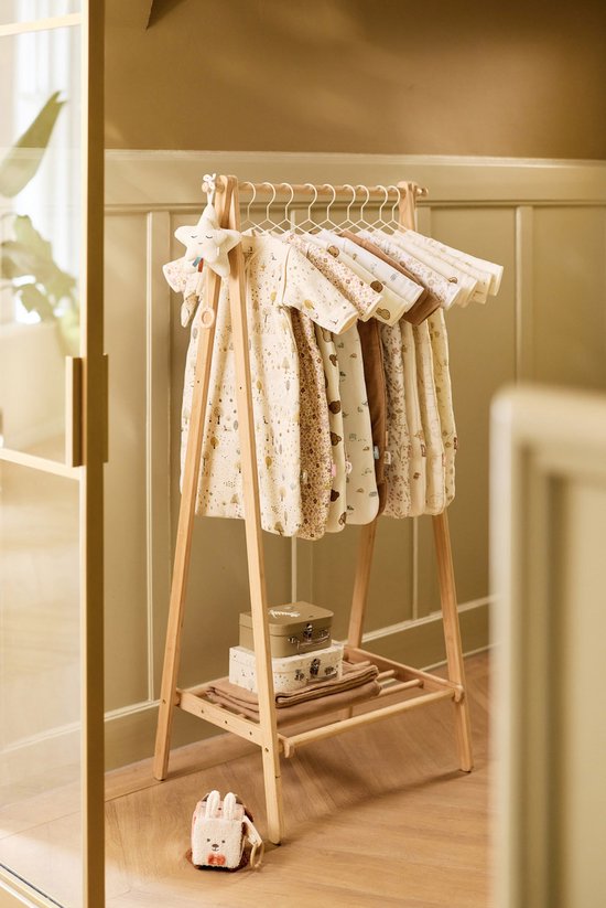 Houten rek met verschillende babykledingstukken, waaronder slaapzakken met diverse prints. Een knuffel ligt op de grond.