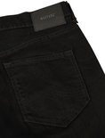 Close-up van de achterkant van een zwarte jeans. De broek heeft een leren Mustang logo met 'True Denim' erop en gestikte achterzakken.