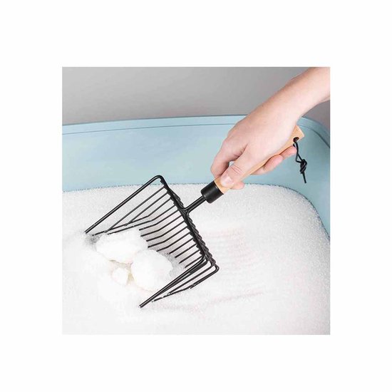 Een hand met een schepje met houten handvat schept klonten uit witte kattenbakvulling.