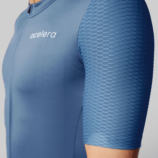Detail van een blauw wielershirt met korte mouwen, met textuur op de mouw en het Acelera logo.