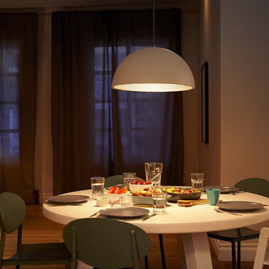 Een gedekte eettafel onder een witte hanglamp, in de avond.