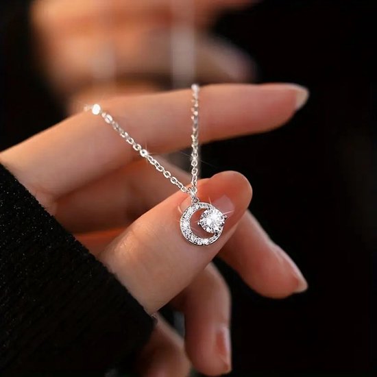 Une femme en pull noir tient un collier argenté avec un pendentif en croissant de lune orné de zirconias.