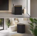 Zwarte wasmand van 160L met gouden accenten en een deksel, staat in een moderne badkamer.