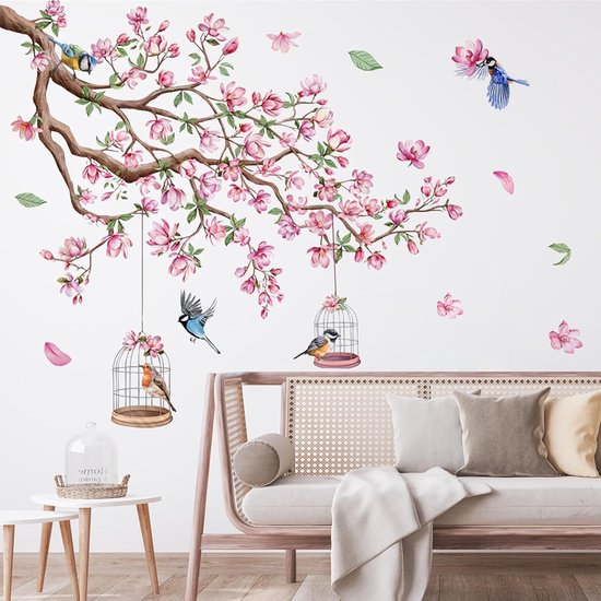 Roze bloesemtakken met vogels en vogelkooien op een witte muur boven een bank.