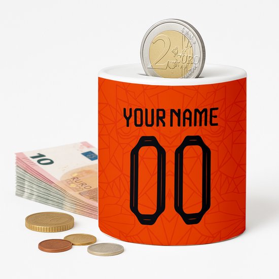Tirelire orange avec design de maillot de football. Personnalisation du nom et du numéro '00'. Une pièce d'un euro dans la fente. Une pile de billets et de pièces à côté.
