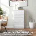 Hoge glanzende witte ladekast met vijf laden, naast een rotan stoel.