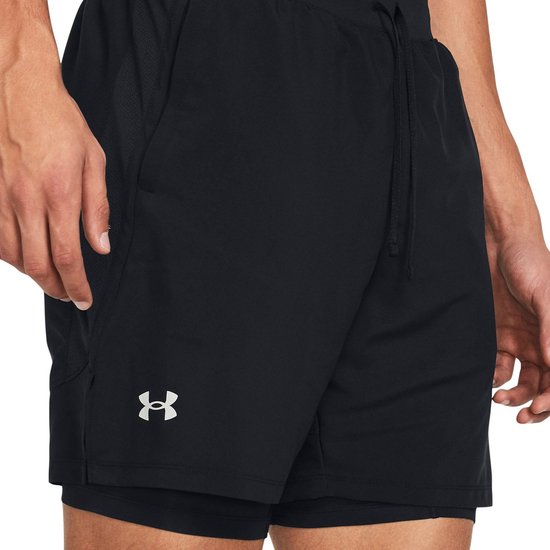 Zijkant van een man in zwarte sportbroek met dubbele laag, met Under Armour logo.