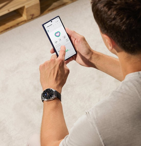 Man met een zilverkleurig slim horloge met zwarte band die naar een telefoon kijkt.