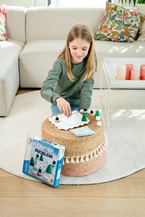 Meisje speelt met "Snow Problem" spel in woonkamer, met doos op bijzettafel.