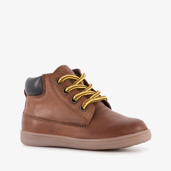 Zijkant van een cognac veterschoen met gele veters en een platte beige zool.