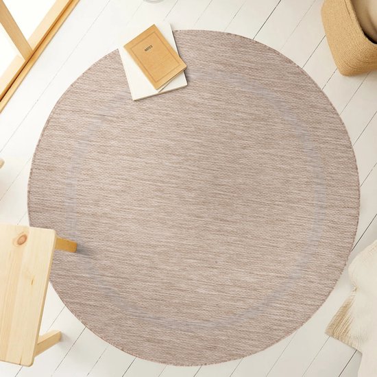 Beige rond vloerkleed in een lichte woonkamer met een boek en een mand.