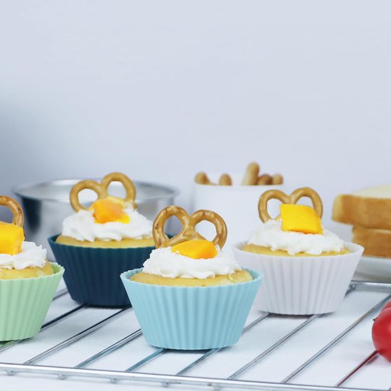 Vier cupcakes met slagroom en een krakeling in blauwe, lichtgroene en witte siliconen vormpjes.