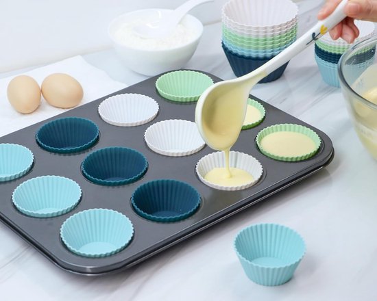 Een bakplaat met blauwe, groene en witte siliconen vormpjes. Deeg wordt in een vormpje gegoten.