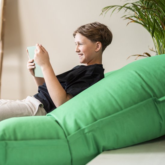 Jongen leest een boek op een groene zitzak.